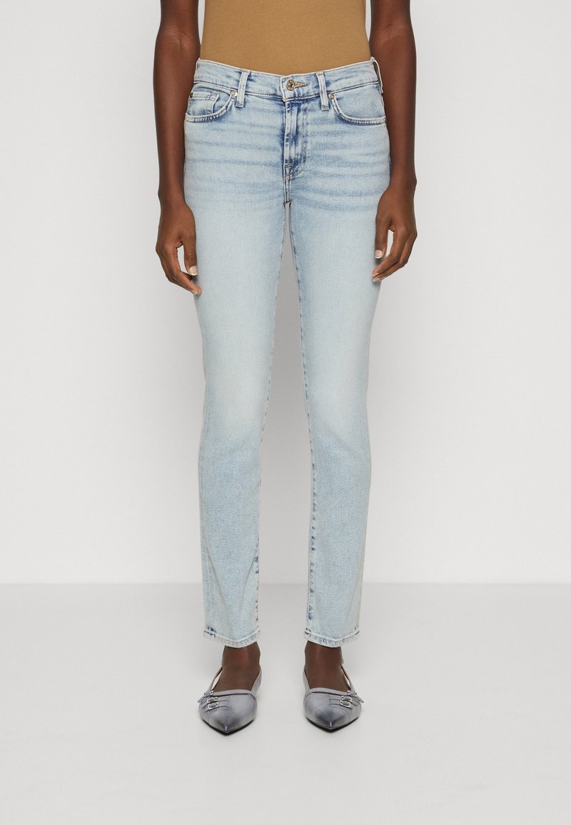 Jeans de mezclilla azul claro con un corte slim, diseño de cinco bolsillos y detalles de desgastado sutil. Combinados con zapatos planos gris de punta afilada.