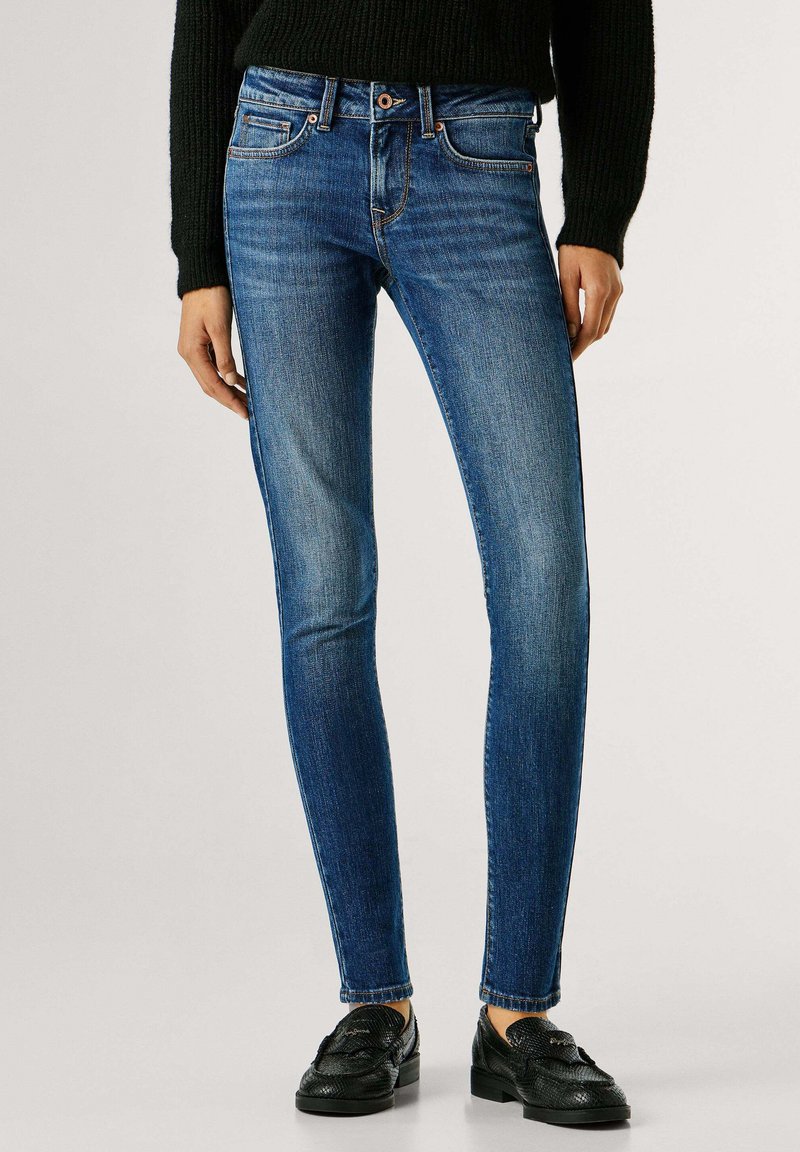 Õhukesed sinised teksad, mis on valmistatud denimist, keskmise vöökohaga, õrna tuhmumisega ja klassikalise viie taskuga ning kombineeritud mustade loaferitega.