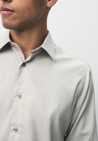 Light grey button-up shirt with a subtle textured pattern and a spread collar. Features two buttons at the collar and a smooth fabric.