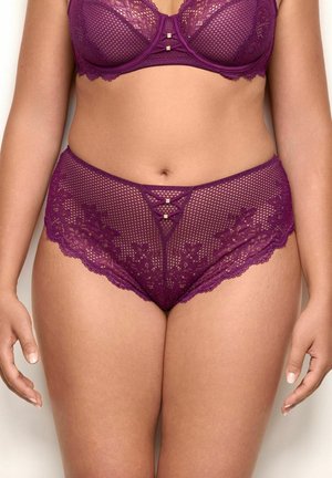 Lilla blonde bh og matchende højtaljede blonde trusser med blomsterdesign, båret af en stående person, vist fra skuldre til øverste lår.