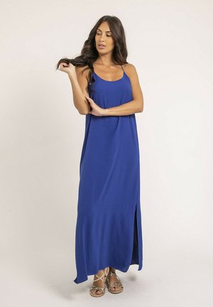 Robe maxi bleue avec des bretelles spaghetti, tissu fluide, fente sur le côté pour faciliter les mouvements et texture douce. Portée avec des sandales élégantes.