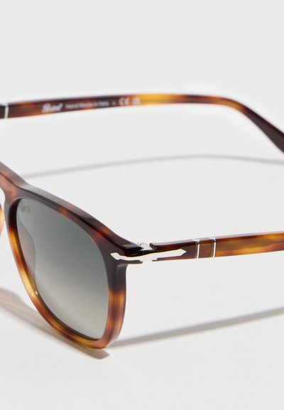 Γυαλιά ηλίου με ταρταρούγα, με σκούρους φακούς με διαβάθμιση και ασημένιες λεπτομέρειες με σχήμα βέλους στη μεριά του βραχίονα.