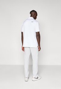 Vit pikétröja med korta ärmar, bakifrån med Nike-logotypen, matchad med ljusgråbyxor och vita sneakers med grå detaljer.