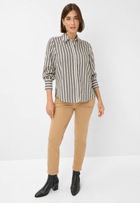 Striped long-sleeve shirt in black and white with a collared neck, paired with beige fitted pants and black ankle boots.