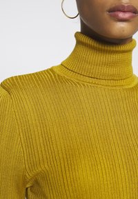 Ribbad, senapsgul polokragetröja som visar en figurnära design med hög krage och texturerad tyg.