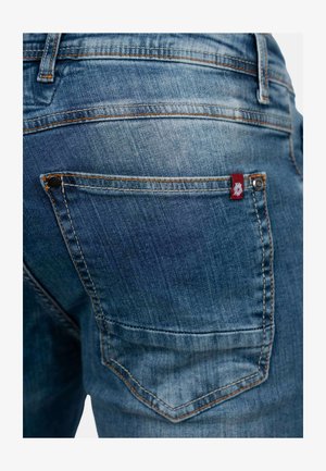 Denim jeans in een medium blauwe was, met oranje stiksels, een achterzak met een rood label en een gladde textuur.