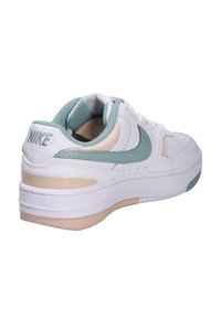 Tenisky Nike v bílé a mátové barvě. Mají hladký kožený svršek, polstrovaný límec a silnou bílou podrážku s béžovým akcentem.