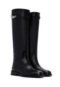 Stivali neri in pelle alti fino al ginocchio con una superficie liscia, punta rettangolare, suola piatta e un accento in metallo argentato vicino alla parte superiore.