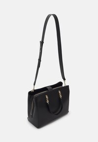 Sac à main rectangulaire noir avec détails en chaîne dorée sur les poignées et une bandoulière réglable, présenté en angle sur fond blanc.