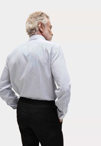 Gestreepte, lichtblauwe en witte overhemd met lange mouwen, voorzien van een puntkraag. Geselecteerd in combinatie met zwarte broeken, die een tailormade pasvorm tonen.