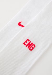 Valged spordisokid, millel on punane Nike'i logo ja "ENG" tekst, ribatud tekstuuriga ning põlveni ulatuva disainiga.