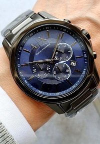 Ümar roostevabast terasest kell, millel on sinine kellakuul, kolm alakuuli ja kuupäeva näidik. Hõbedased tunni indekserid ja metallist käevõru.