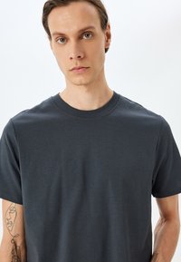 Camiseta de algodón gris oscuro con mangas cortas, cuello redondo y una textura suave, que presenta una silueta ajustada sin patrones o elementos metálicos visibles.