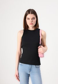 Top sin mangas negro acanalado con cuello alto, combinado con jeans ajustados de color azul claro. La modelo sostiene un pequeño bolso rosa con una correa.
