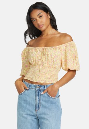Schulterfreies gelbes Blumenshirt mit kurzen Puffärmeln, gerafftem Halsausschnitt und gerafftem Bund. Getragen mit hochtaillierten hellblauen Jeans.