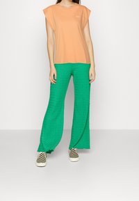 Oranžový krátký rukáv s kulatým výstřihem, spárovaný se zelenými strukturovanými širokými kalhotami. Outfit doplňují černobílé kostkované boty.