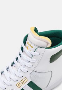 Sneaker alta con una tomaia in pelle bianca, dettagli verdi e pannelli in rete testurizzata. Fodera del colletto gialla e lacci bianchi. Dettaglio del logo in oro.