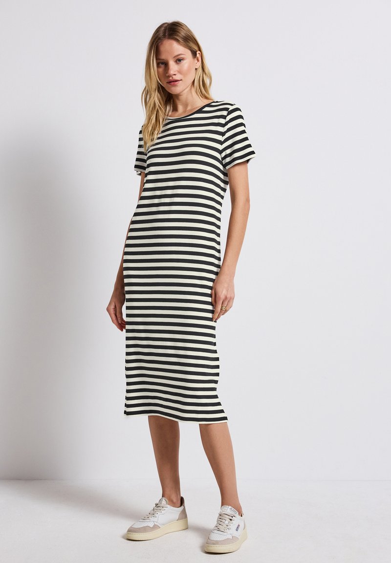 Striped midi dress in black and cream, made of soft fabric with a round neckline and short sleeves, paired with white sneakers.