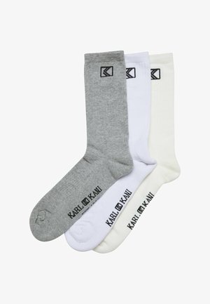Tre par sokker i grå, hvid og off-white farver, lavet af strikmateriale, med sort logo og tekst ved kanten.