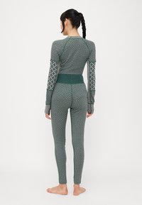 Top de manga larga de patrón verde y leggings con puños y cinturilla acanalados. Presenta diseños intrincados en tonos de verde más claros.
