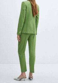 Blazer vert cintré et pantalon assorti en tissu texturé. Le blazer est orné de boutons. Porté avec des chaussures pointues vert clair.