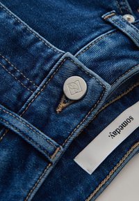 Dunkelblaue Jeans aus Denim mit einer silbernen Knopf mit Logo, sichtbaren Nähten und einem weißen Stoffetikett mit der Aufschrift "someaday".
