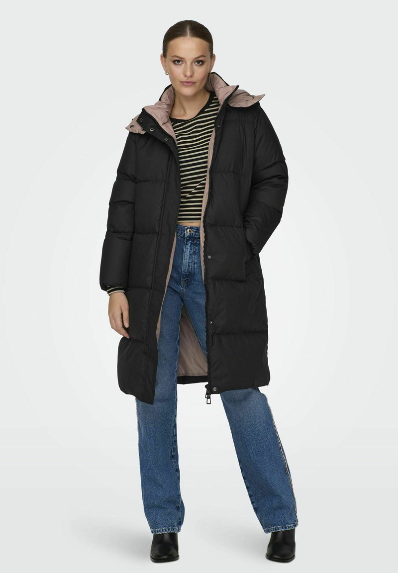 Svart pufferjakke med rosa fôr, til kneet, med glidelås, lommer og hette, kombinert med stripet topp og blå jeans.