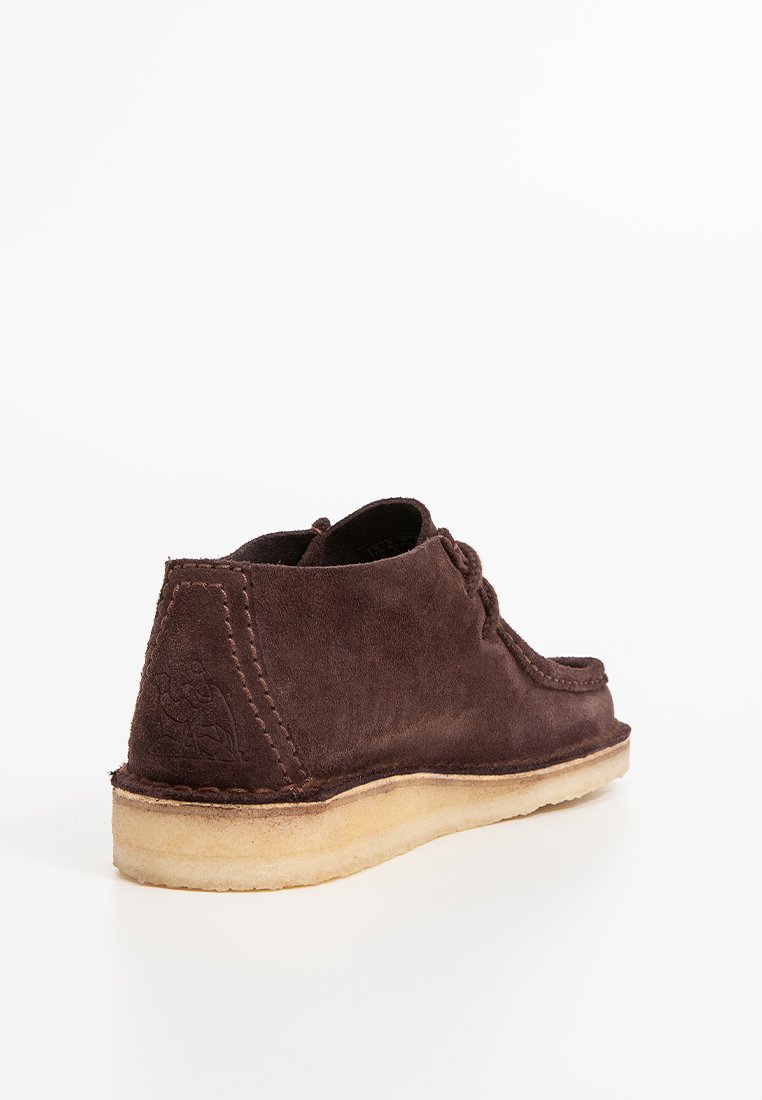 Braune Wildlederschuhe mit niedrigem Profil, runder Zehenpartie und kontrastierender heller Sohle. Sie verfügen über gestickte Details und ein geprägtes Logo auf der Rückseite.