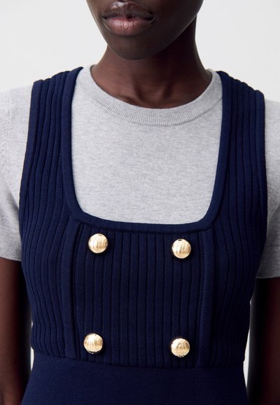 Robe en tricot côtelé marine avec un décolleté carré, comportant quatre boutons dorés sur le buste, associée à un haut gris à manches courtes.