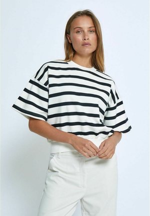 White shirt with black horizontal stripes, round neckline, and wide short sleeves. Paired with light-colored fitted trousers.