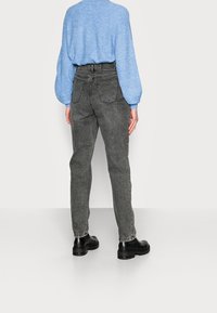 Vaqueros grises de cintura alta con corte recto, que presentan bolsillos traseros y costuras en contraste. Combinados con un suéter texturizado de color azul claro.