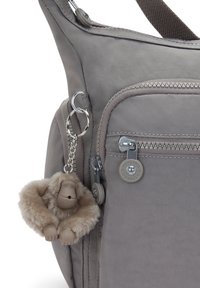 Graue Stoff-Schultertasche mit einem Reißverschlussfach und einem dekorativen Affen-Schlüsselanhänger. Verfügt über eine strukturierte Oberfläche und metallische Hardware-Details.
