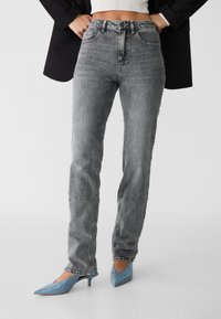 Grå högmidjade jeans med en urblekt textur, rak benstorlek, femfickdesign och en subtil fransad fåll. Matchat med ljusblå klackar.