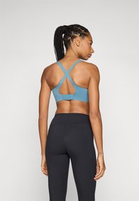 Sujetador deportivo azul con un acabado texturizado, tirantes cruzados y un corte circular en la parte posterior. Combinado con leggings negros de cintura alta.