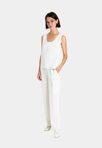 Top bianco senza maniche con scollatura a barca e dettagli con bottoni, abbinato a pantaloni cargo a gamba larga con tasche laterali e una vestibilità comoda.