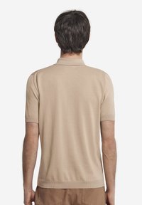 Beige kortärmad polo med en mjuk textur, med klassisk krage och ribbade ärmslut, visad bakifrån.