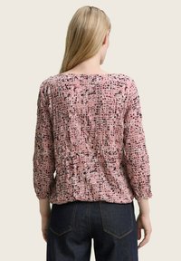 Rosa gemusterte Bluse mit langen Ärmeln, die eine strukturierte Oberfläche und subtile schwarze Akzente aufweist. Der Rücken hat einen runden Ausschnitt und eine geraffte Detailgestaltung.