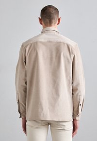 Cămașă bej cu nasturi, confecționată dintr-un material moale și texturat. Aceasta are un guler și m�âneci cu manșete, cu un croi ușor relaxat și un design minimalist.