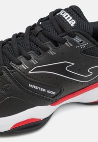 Zapatilla deportiva negra con parte superior de malla, acentos sintéticos texturizados y suela de goma roja y blanca con la marca "MASTER 1000".