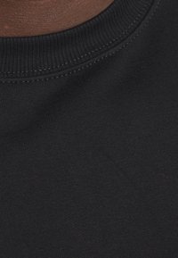 Camiseta negra de algodón con cuello redondo acanalado y textura suave. Vista en primer plano que resalta el acabado uniforme del material.