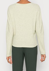 Lichtgroene, getextureerde gebreide top met een comfortabele pasvorm, ruime halslijn en lange mouwen. De zoomlijn is iets gebogen en past mooi bij de donkergroene broek.