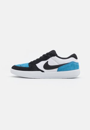 Lavtopsneaker med sorte, hvide og blå ruskindspaneler, sort Nike-swoosh, sorte snørebånd og hvid gummisål mod en hvid baggrund.