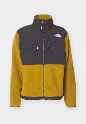 Polarowy jacket z czarną górą i żółtymi dolnymi sekcjami. Posiada wysoki kołnierz, zamek z przodu oraz dwie boczne kieszenie, w tym jedną kieszeń na piersi zapinaną na zamek.