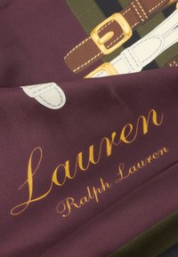 Hedvábný šátek s vínovým pozadím, zdobený potiskem pásků a zlatých kovových doplňků. Nápis „Lauren Ralph Lauren“ je výrazně zobrazen žlutým písmem.