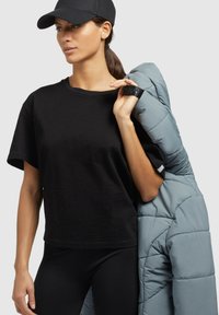 Čierne tričko s krátkym rukávom, čierne legíny a svetlošedá prešívaná bunda prehodená cez plece. Bunda má prešívaný vzor.