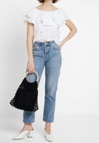 Vit rynkad blus med hållet detaljer, blå högmidjade jeans, svart flätad handväska med trähandtag och vita klackskor.