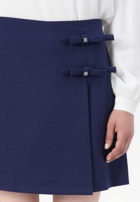 Navy blue skirt made of textured fabric, featuring two bow accents on the left side, with a diagonal fold design.