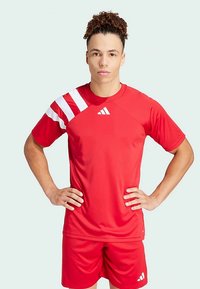 Red athletic jersey with white striped accents on the left shoulder, round neck, and matching red shorts. Polyester material, smooth texture.