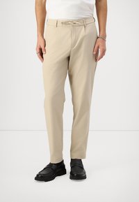 Beige kalhoty s volným střihem, elastickým pasem a detaily na šňůrku. Nosené s černými botami, které mají hladký povrch a pevné podrážky.