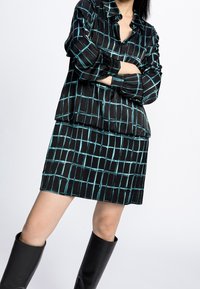 Outfit a scacchi neri e teal composto da una camicia con bottoni e una gonna abbinata. Il tessuto ha una texture liscia, con maniche lunghe e una vestibilità rilassata.